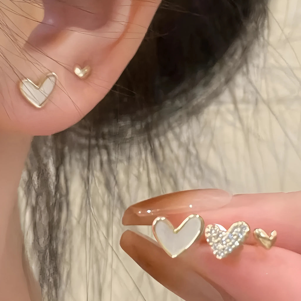 Three pairs of heart-shaped earrings in gold, black, pink, and black white colours with love-themed girly styling
