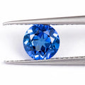 A royal blue loose gemstone with a precision cut, shown against a neutral background.
