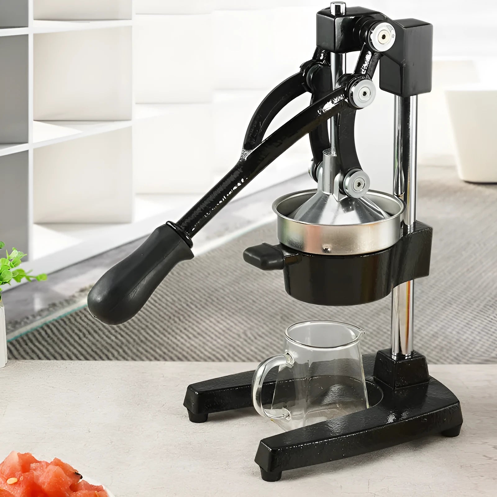 Black or white cast iron manual citrus juicer with stainless steel funnel on a kitchen counter.