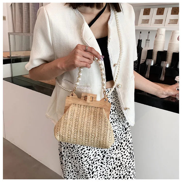 Women's woven straw shoulder bag with pearl chain strap in beige, showing its horizontal square shape.