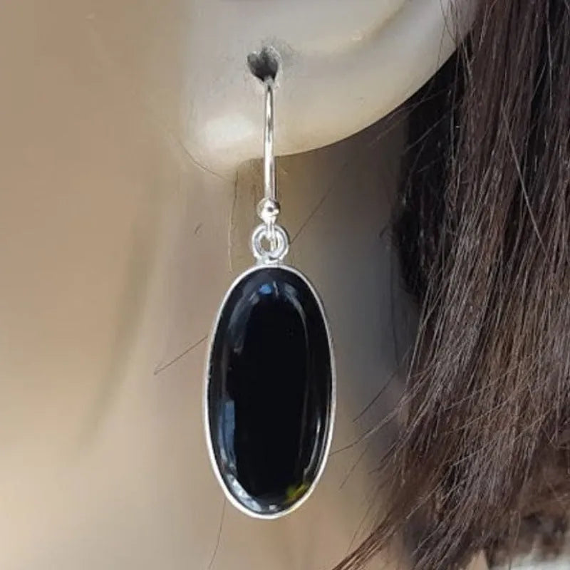 Close-up of women's earrings with black agate oval pendant and silver electroplated geometrical alloy design.