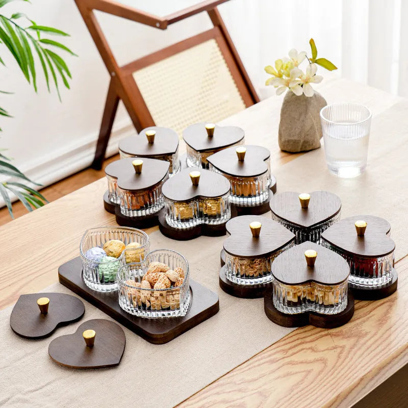 Clear glass serving platter with heart-shaped compartments and a transparent lid on a table.