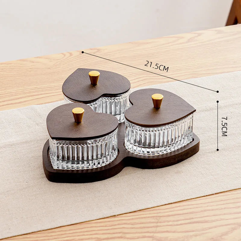Clear glass serving platter with heart-shaped compartments and a transparent lid on a table.