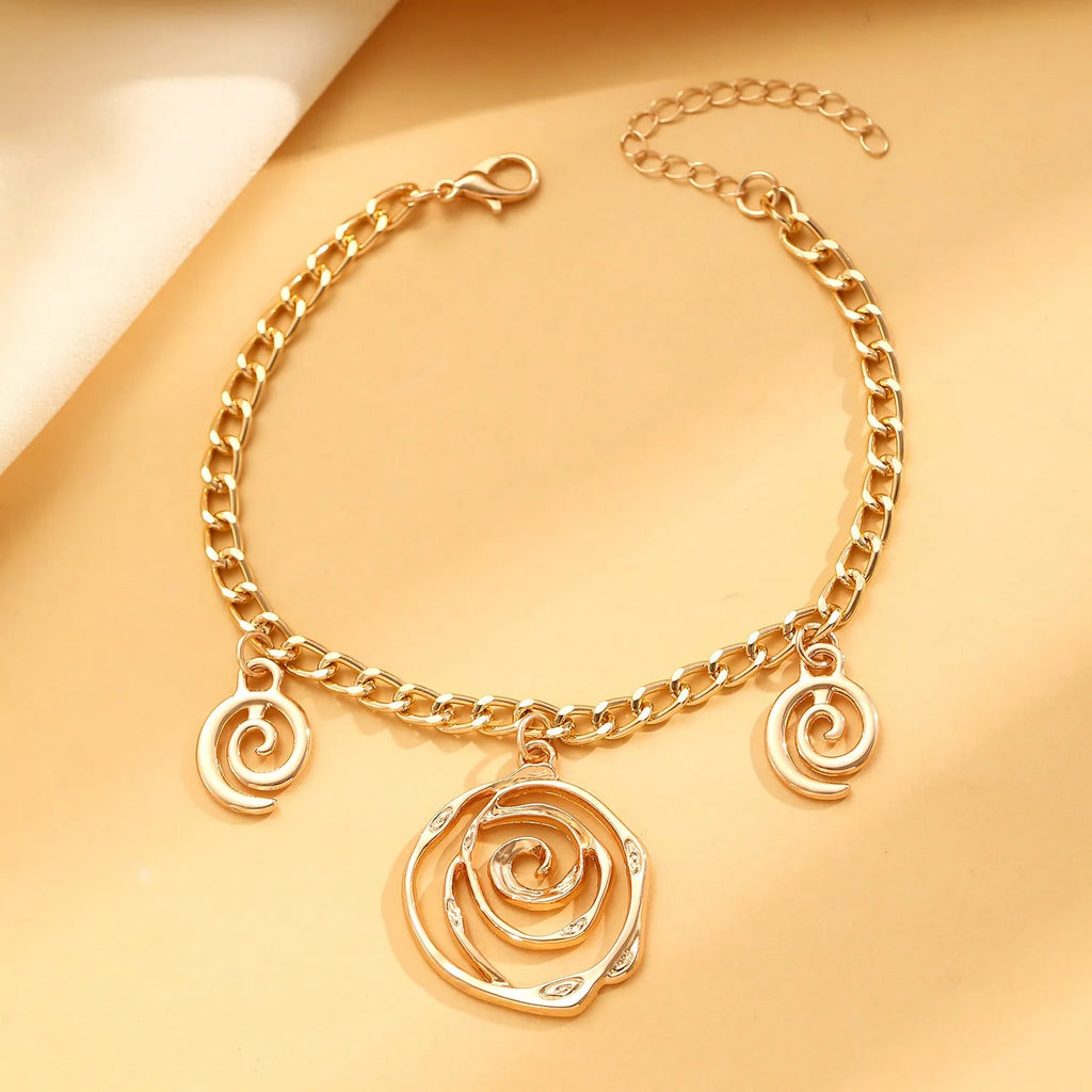 Geometric spiral donut jewellery set with gold necklace, bracelet, and ear hooks on dark background