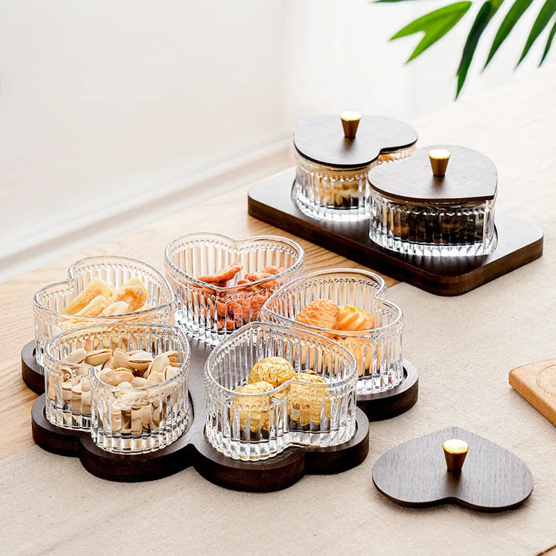 Clear glass serving platter with heart-shaped compartments and a transparent lid on a table.
