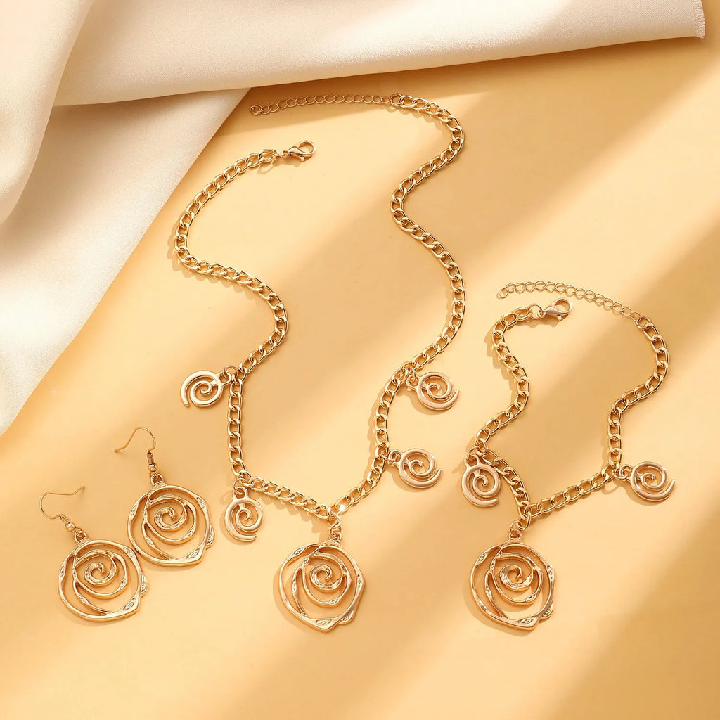Geometric spiral donut jewellery set with gold necklace, bracelet, and ear hooks on dark background