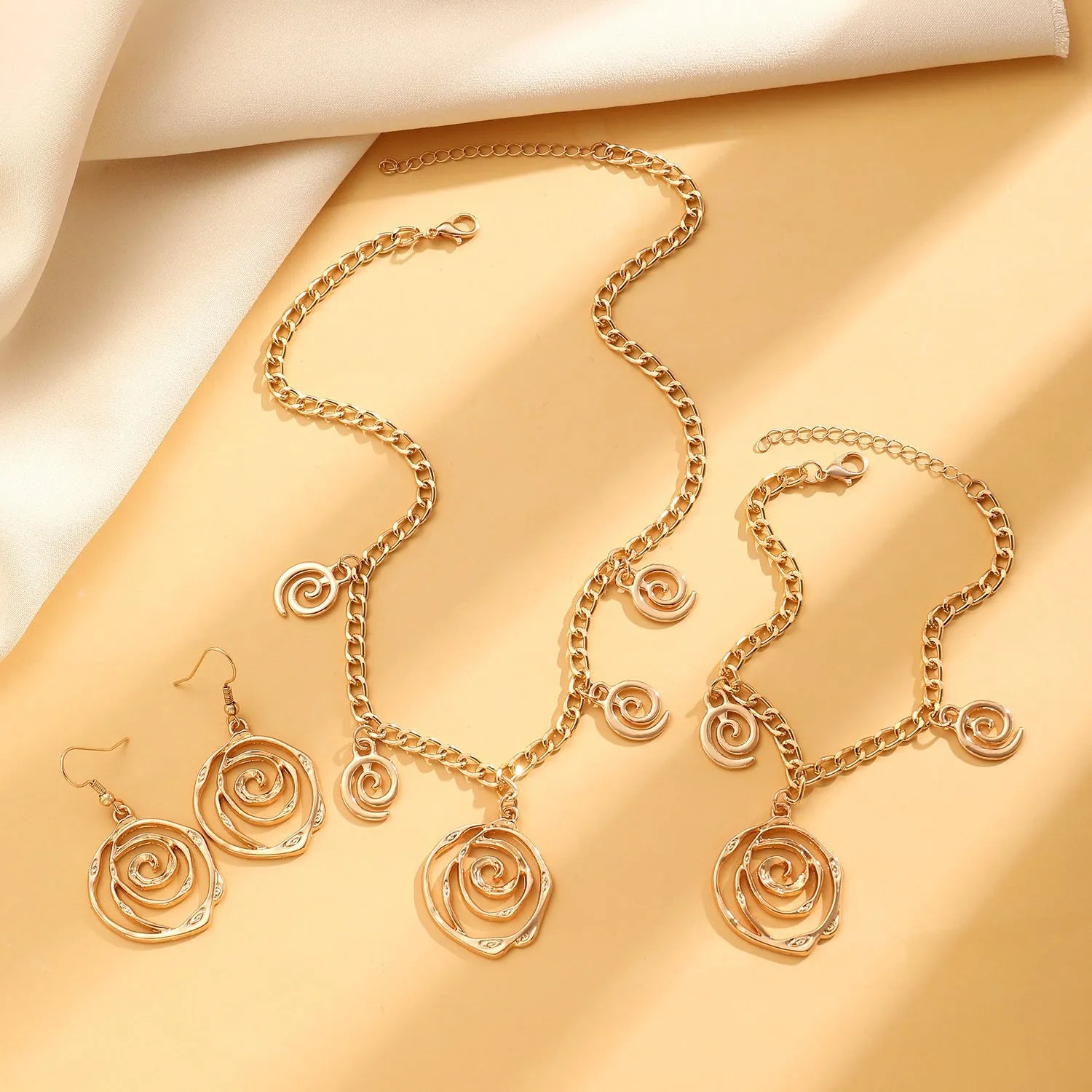 Geometric spiral donut jewellery set with gold necklace, bracelet, and ear hooks on dark background