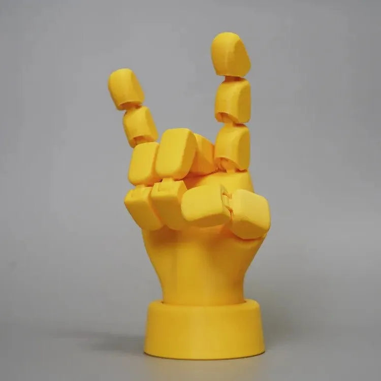 Yellow 3D printed hand prop with movable joints on a plain background.