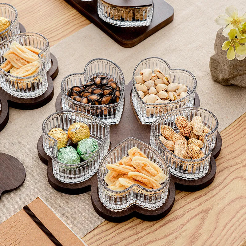 Clear glass serving platter with heart-shaped compartments and a transparent lid on a table.