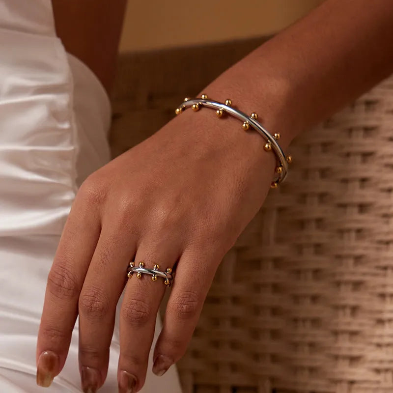 Stainless steel alloy C-shaped bracelet with textured rivet design and bean beads on an adjustable clasp.