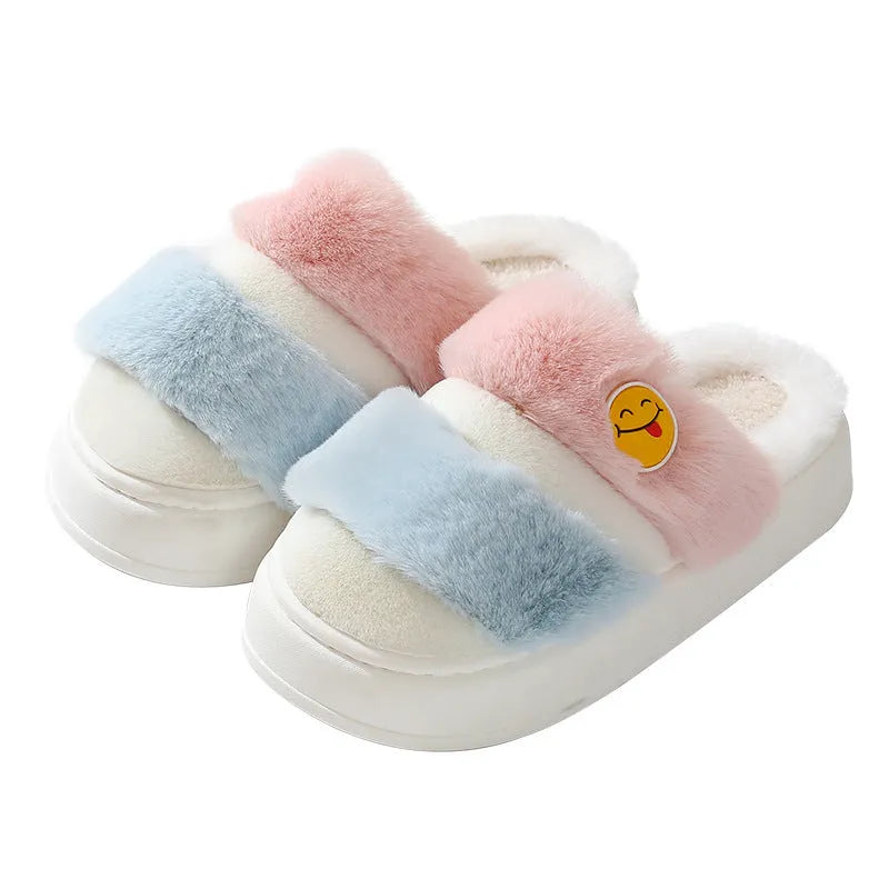 Pair of pink and green cartoon-style plush winter slippers with a cashmere lining on a wooden floor.