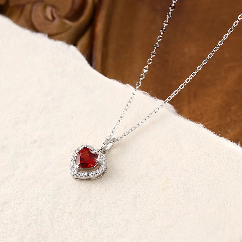 Heart-shaped sterling silver necklace with a round amethyst gemstone on a cross chain.