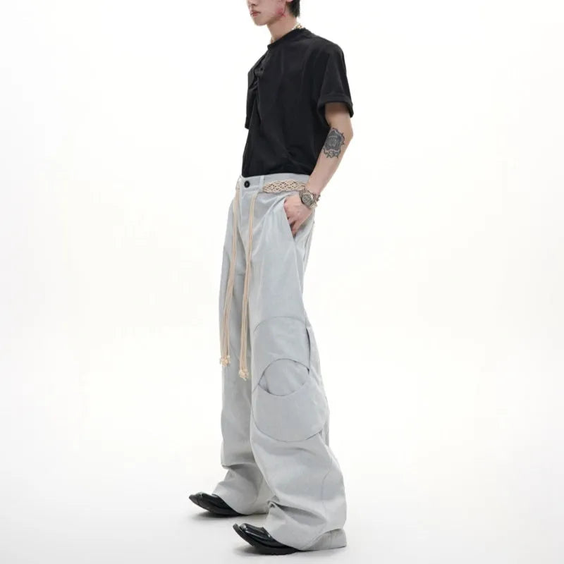 Men's dark blue straight-leg jeans showing heavy 3D stitching and tassel pocket decoration.