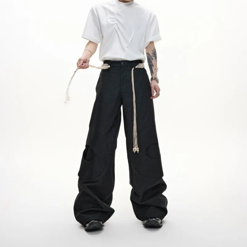 Men's dark blue straight-leg jeans showing heavy 3D stitching and tassel pocket decoration.