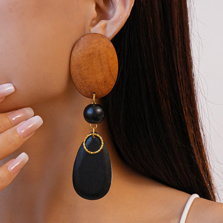 Close-up of handmade brown and black wooden ellipse earrings with silver needle fastenings on a textured background.