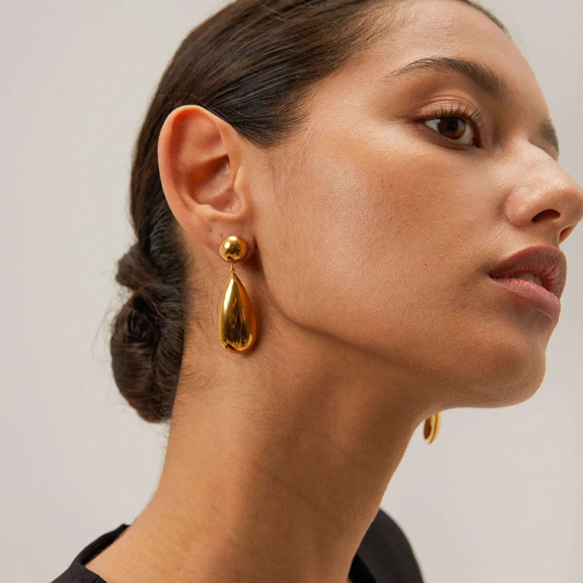 Gold-coloured stainless steel earrings featuring a geometric hemisphere shape with a dangling water drop pendant.