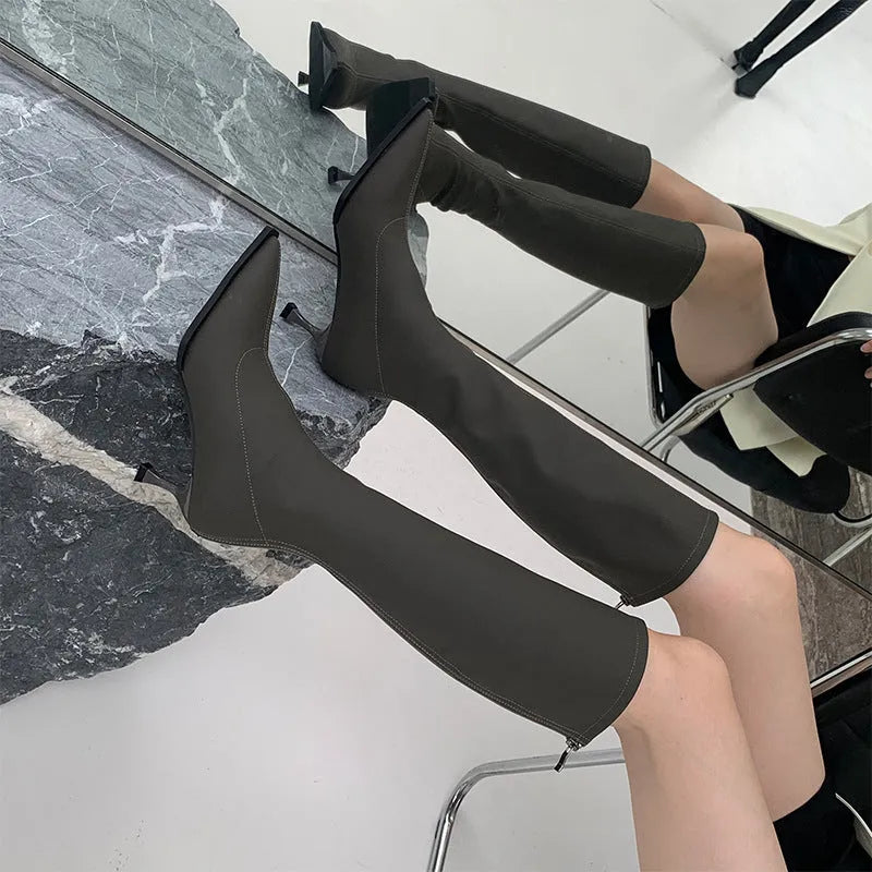 Black pointed toe below the knee women's boots with a stiletto heel and back zipper closure on a white background.