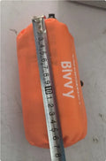 Portable orange disaster relief tent with sleeping bag and emergency blanket setup outdoors