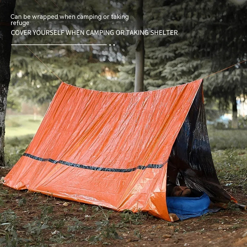 Portable orange disaster relief tent with sleeping bag and emergency blanket setup outdoors