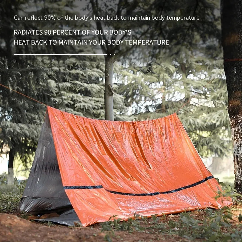 Portable orange disaster relief tent with sleeping bag and emergency blanket setup outdoors
