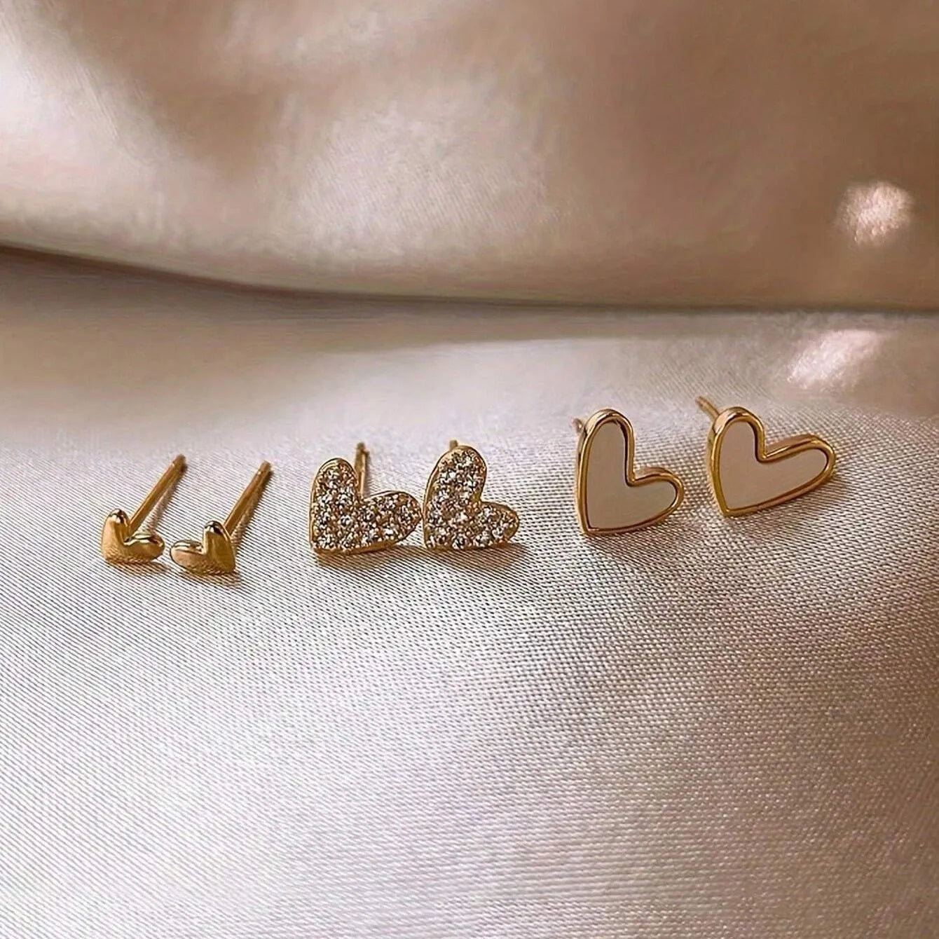 Three pairs of heart-shaped earrings in gold, black, pink, and black white colours with love-themed girly styling