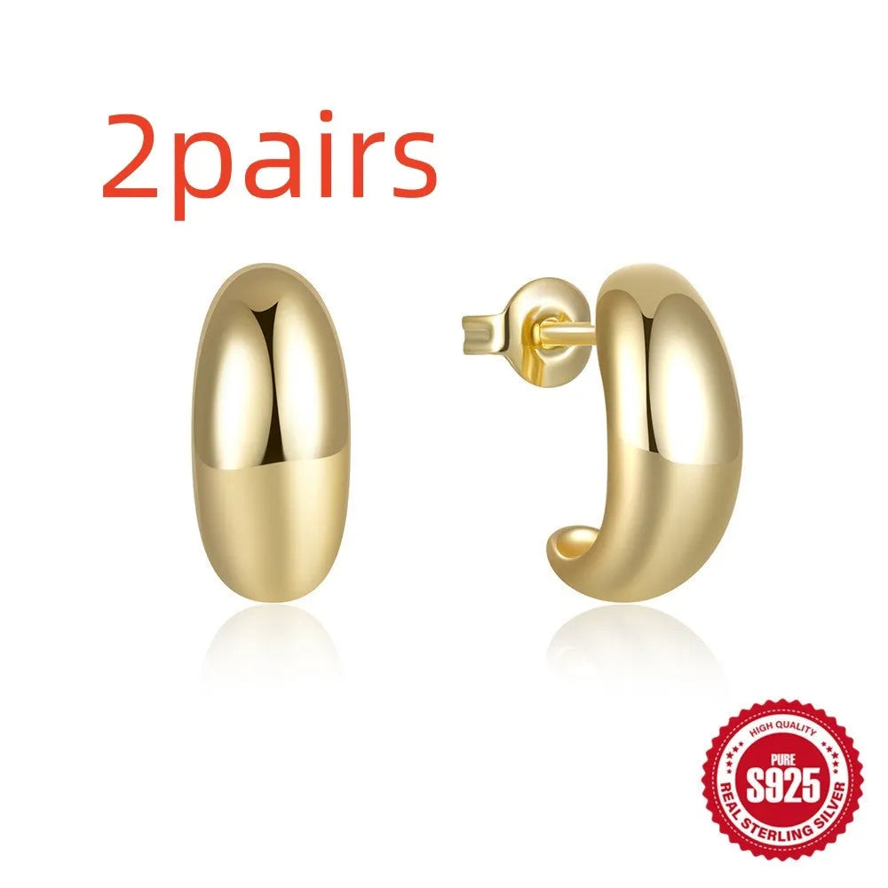 Close-up of a glossy C-shaped sterling silver stud earring with a gold electroplated finish.