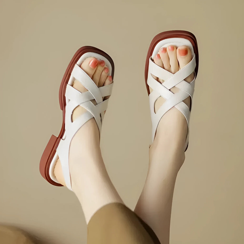 Women's glossy patent leather sandals with cross-belt straps, square toe, and a low block heel.