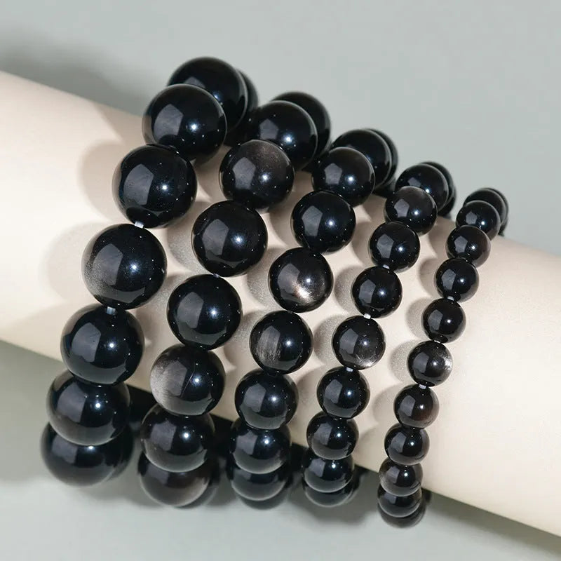 Hand-woven round obsidian bracelet with crystal beads in various colour options on a wrist.