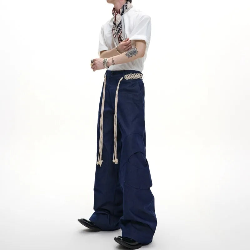 Men's dark blue straight-leg jeans showing heavy 3D stitching and tassel pocket decoration.
