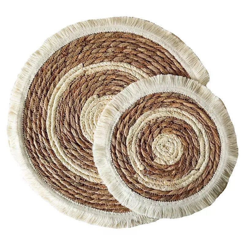 Round natural papyrus straw placemat with decorative tassel edge on a wooden table.
