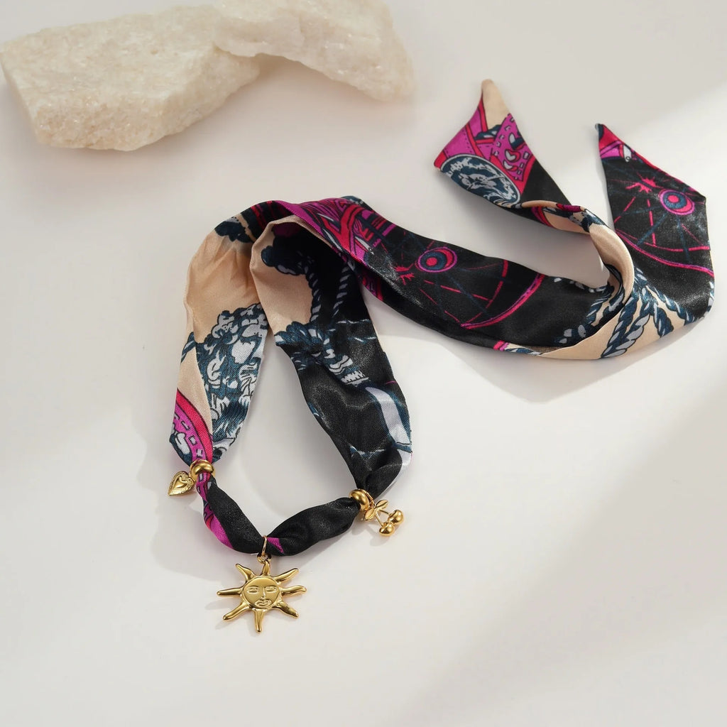 Geometric sun pendant on a gold chain, shown as both a women's necklace and bracelet on a grey background.