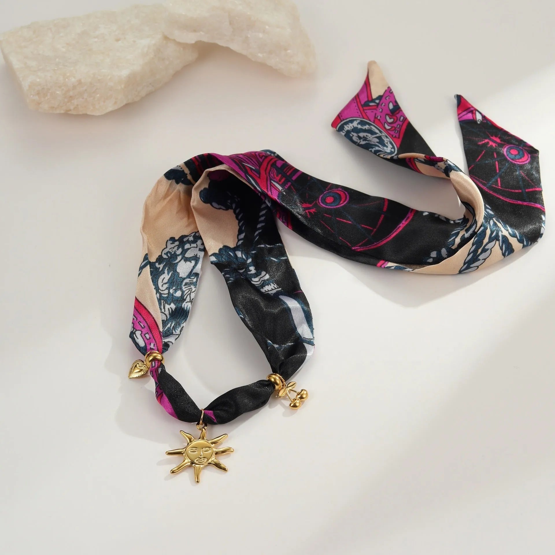Geometric sun pendant on a gold chain, shown as both a women's necklace and bracelet on a grey background.
