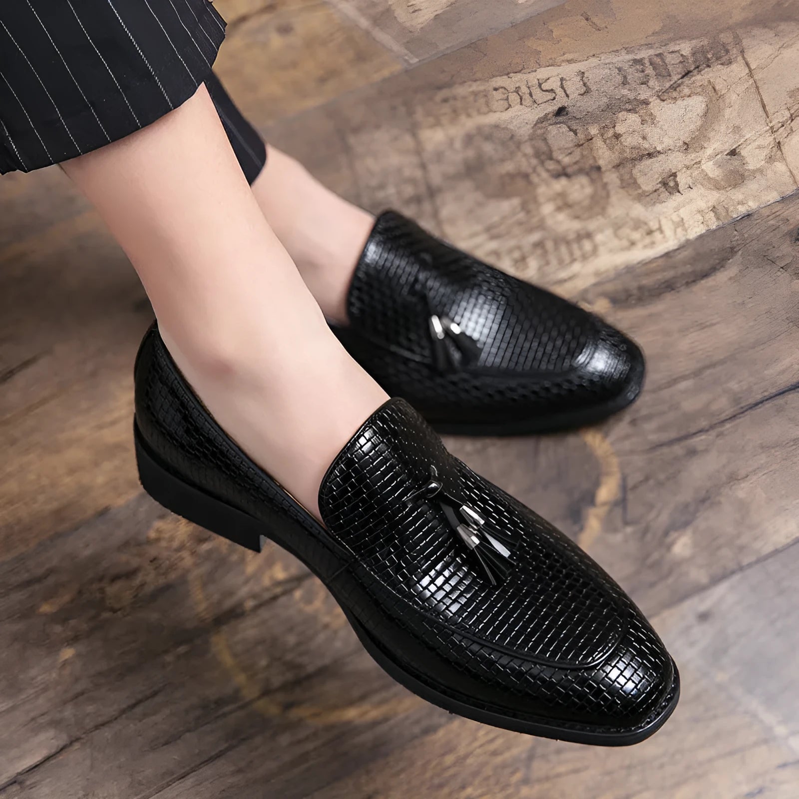 Men's black pointed toe slip-on shoes with a tassel detail on the front.