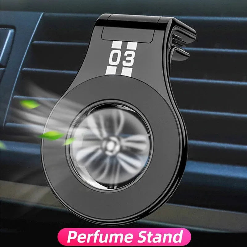 Black magnetic car phone holder clipped to a car air vent, holding a mobile phone, with a fragrant slice inserted.