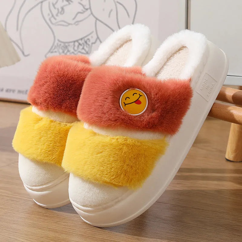 Pair of pink and green cartoon-style plush winter slippers with a cashmere lining on a wooden floor.