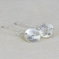 Silver-coloured women's earrings with a glossy round bird and flower design on a white background.