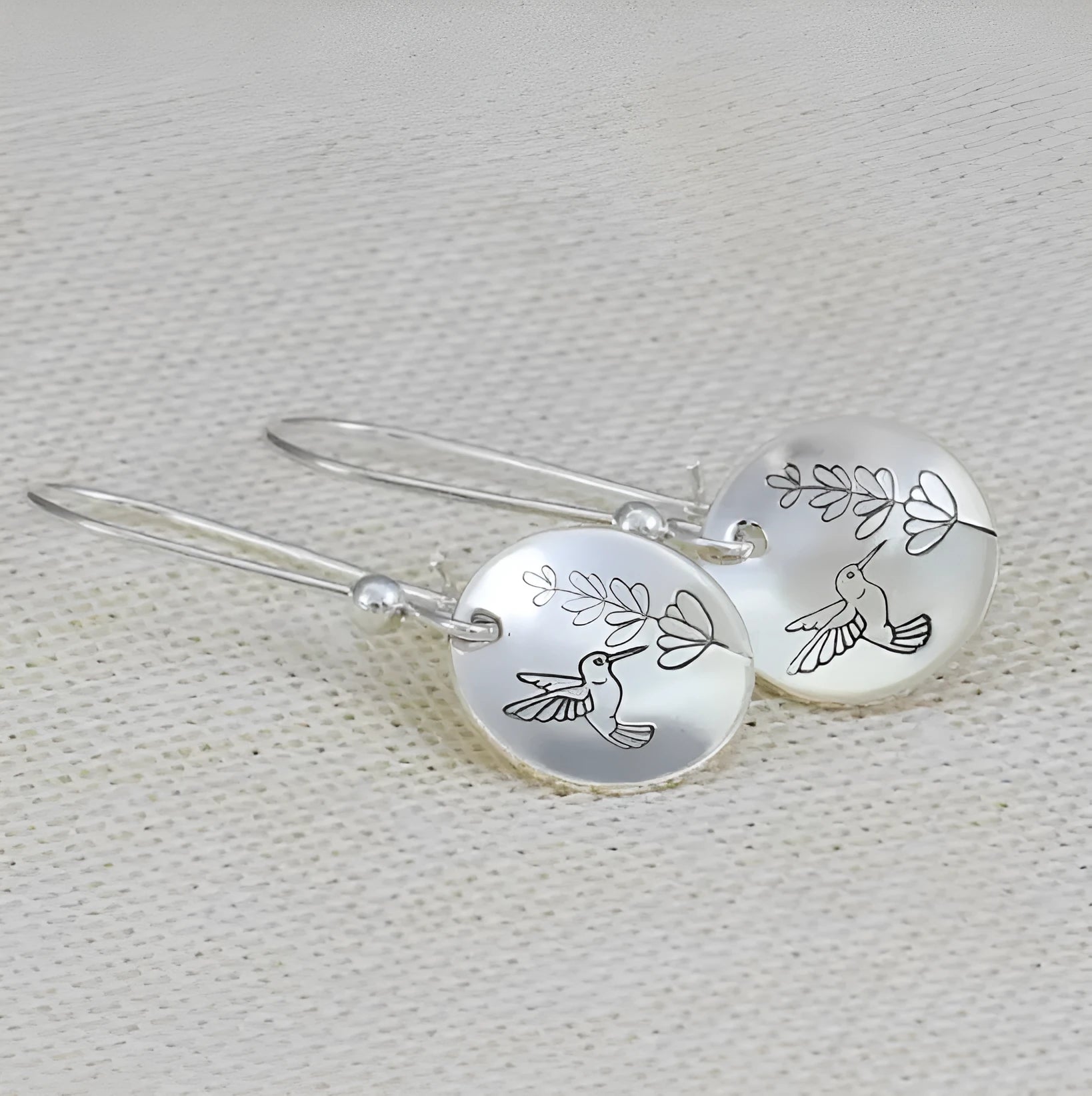 Silver-coloured women's earrings with a glossy round bird and flower design on a white background.