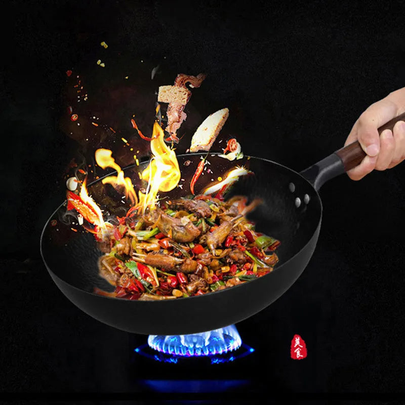 Black traditional handmade iron wok pan with a long wooden handle on a kitchen hob.