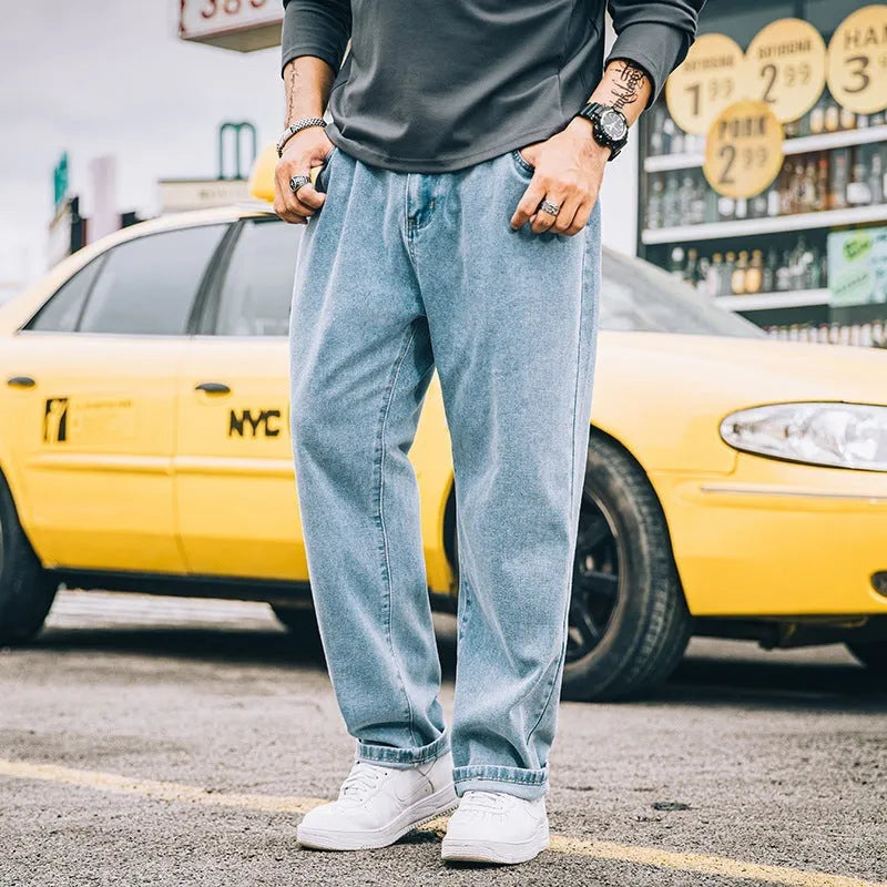 Men's loose straight-cut blue jeans on a plain background, showing the mid waist and zipper fly detail.