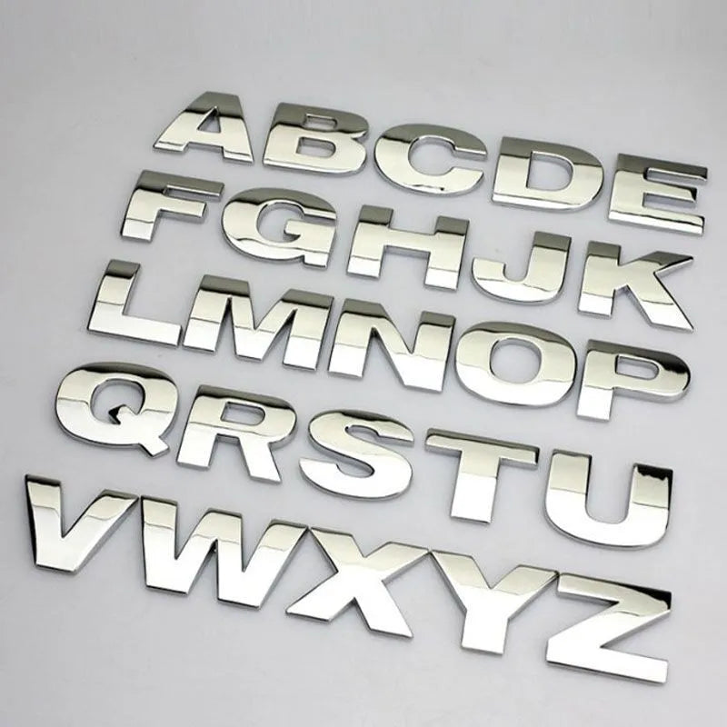 Close-up of a silver metal 3D letter 'A' car sticker with adhesive backing, shown next to a black version.