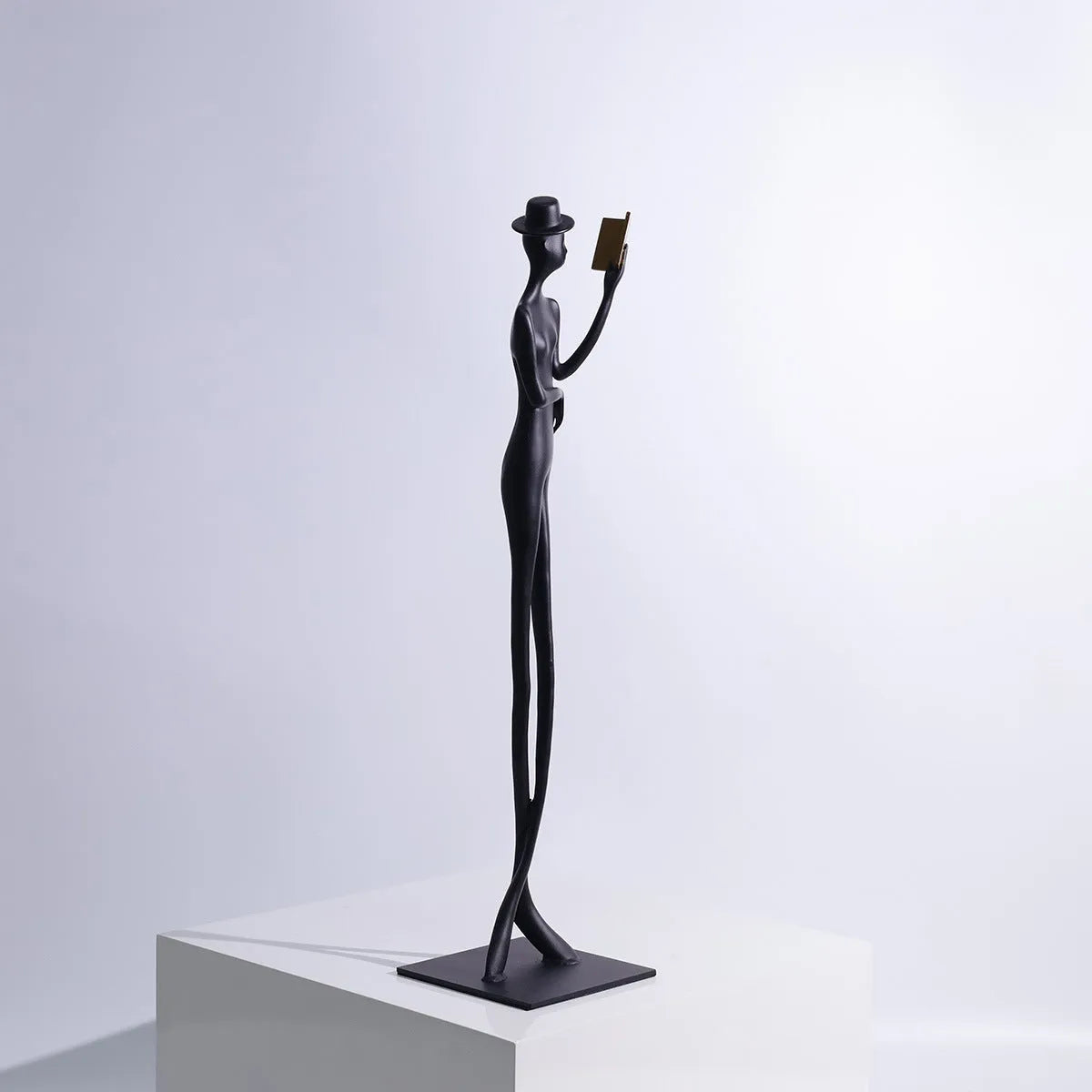 Black cast aluminium sculpture of a reading woman on a desktop, 51 cm tall.