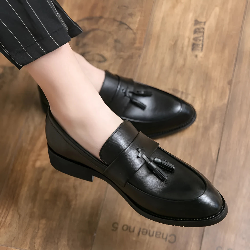 Men's black slip-on business casual shoes with a tassel detail and pointed toe.