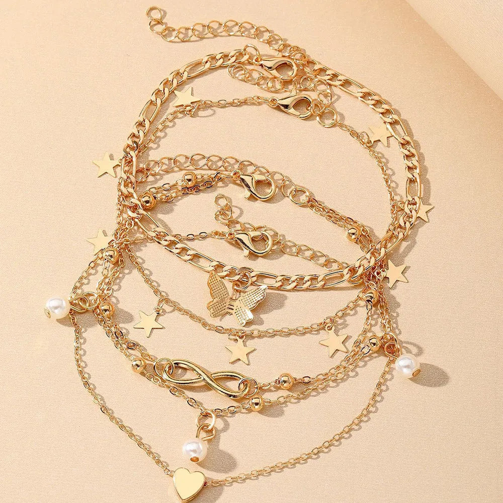 Four alloy anklets with butterfly, pearl and heart charms arranged as a layered jewellery set