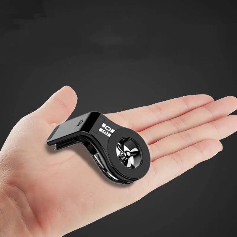 Black magnetic car phone holder clipped to a car air vent, holding a mobile phone, with a fragrant slice inserted.