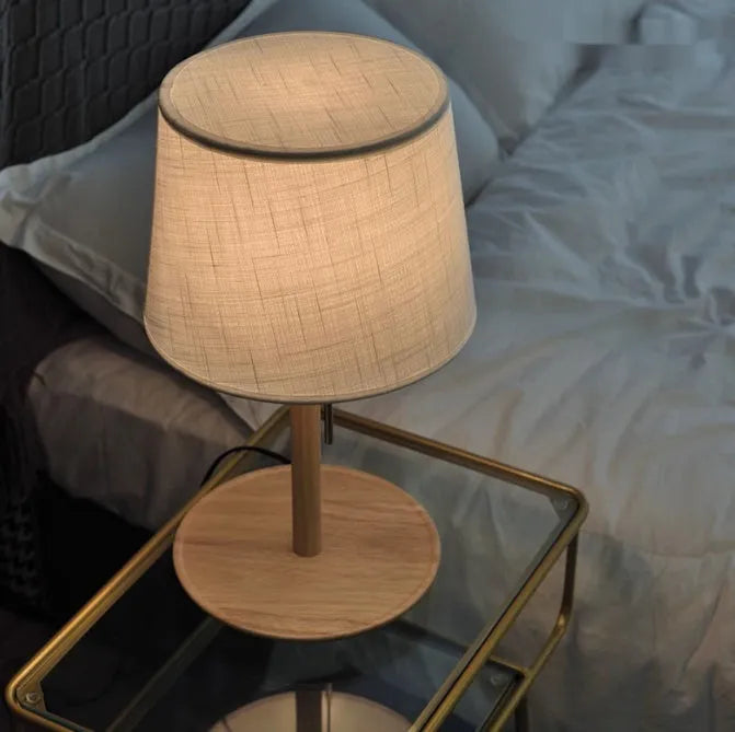 Walnut colour solid wood bedside lamp with a white fabric lampshade and a black cable switch.