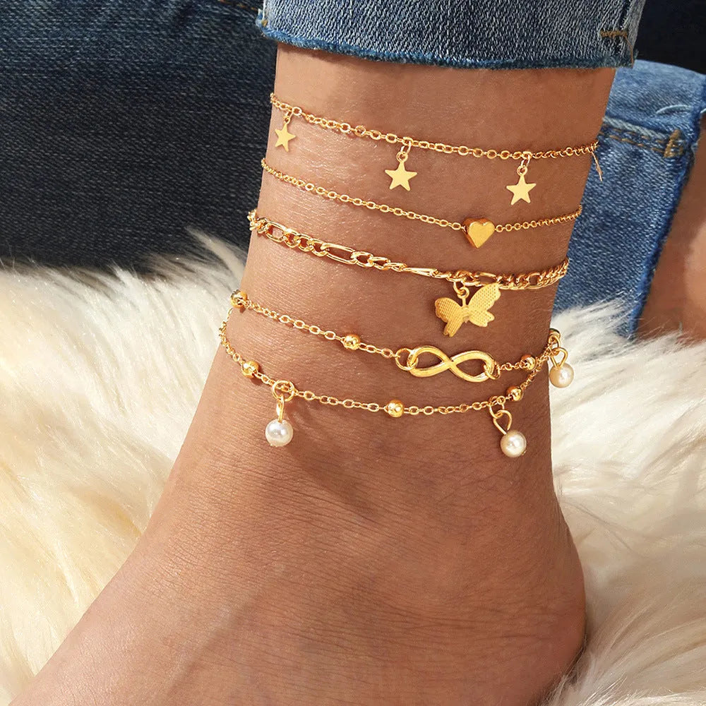 Four alloy anklets with butterfly, pearl and heart charms arranged as a layered jewellery set