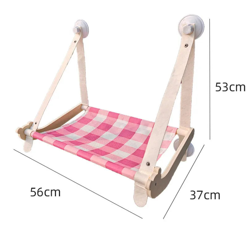 Pink wooden cat hammock bed with suction cups attached to a window, showing a cat lying on the linen mat.