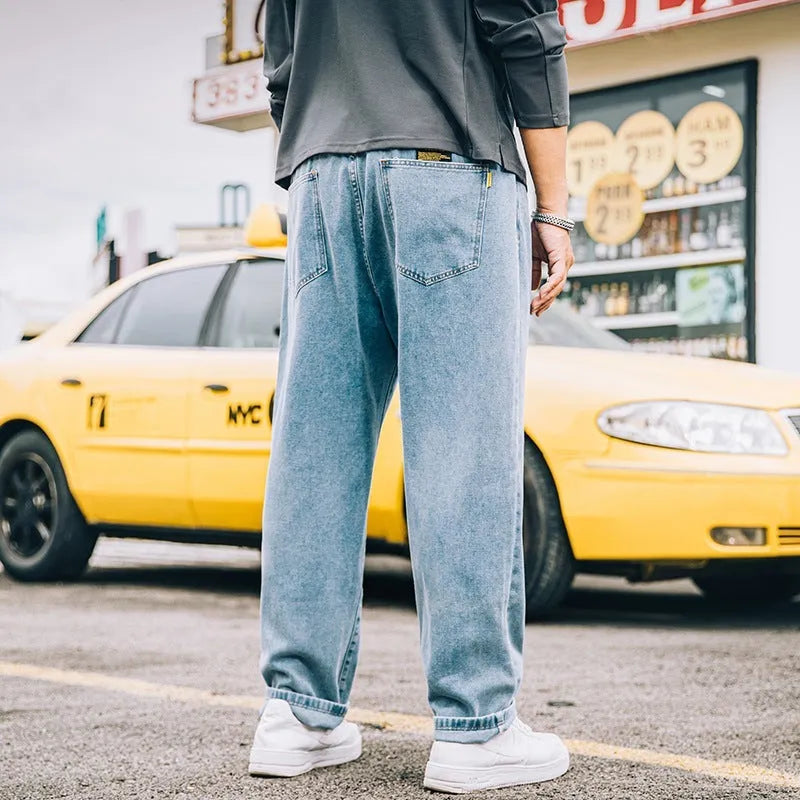 Men's loose straight-cut blue jeans on a plain background, showing the mid waist and zipper fly detail.
