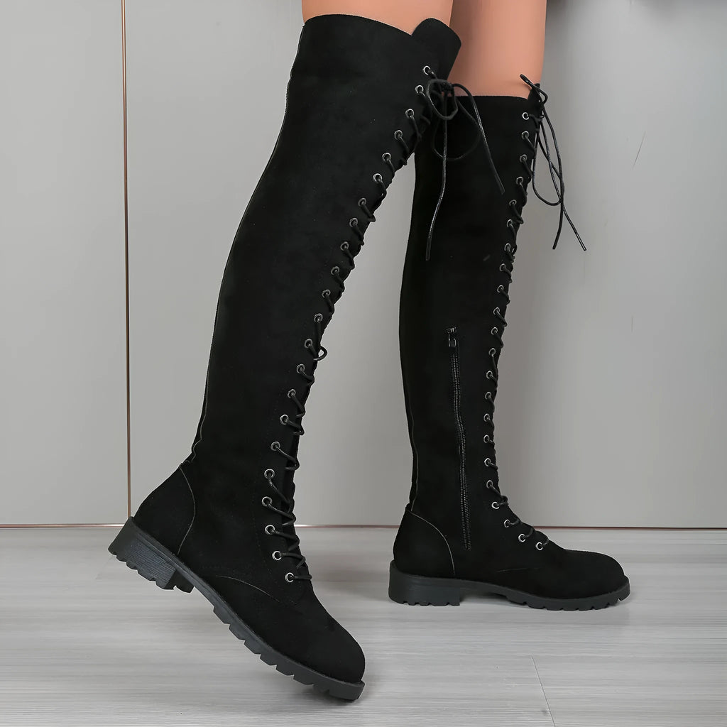 Black lace-up over the knee boots with round toe and flat rubber sole on a neutral background.