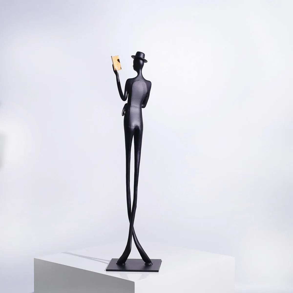 Black cast aluminium sculpture of a reading woman on a desktop, 51 cm tall.
